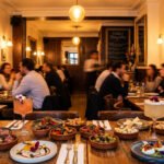 Restaurant Biotiful Batignolles. Table avec tapas variés, cocktails. Clients en discussion, ambiance chaleureuse, lumières tamisées.