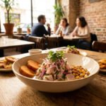 Gros plan sur un bol de ceviche équatorien avec patates douces et maïs grillé, accompagné de bananes plantains frites. Des clients déjeunent en arrière-plan.