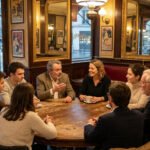 Un groupe de sept personnes débat autour d'une table en bois dans un café parisien classique avec miroirs et vue sur la rue.