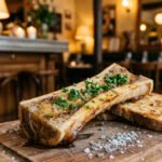 Un os à moelle rôti servi sur une planche en bois avec du persil et du pain grillé, dans un restaurant chaleureux.