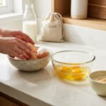 Gros plan sur des mains préparant une recette. Sur un comptoir, des œufs entiers et battus, lait, sucre, crème vanille et cannelle.