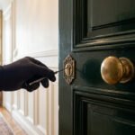 Main gantée ouvrant une serrure sur une porte vert foncé dans un appartement parisien lumineux.