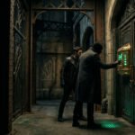 Scène d'escape game Batman. Deux hommes face à une porte sombre avec un puzzle lumineux vert et un symbole du Sphinx.