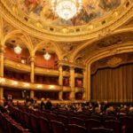 Vue panoramique de l'intérieur richement décoré d'un opéra parisien, avec ses balcons dorés, sièges rouges et lustres scintillants, avant un spectacle.